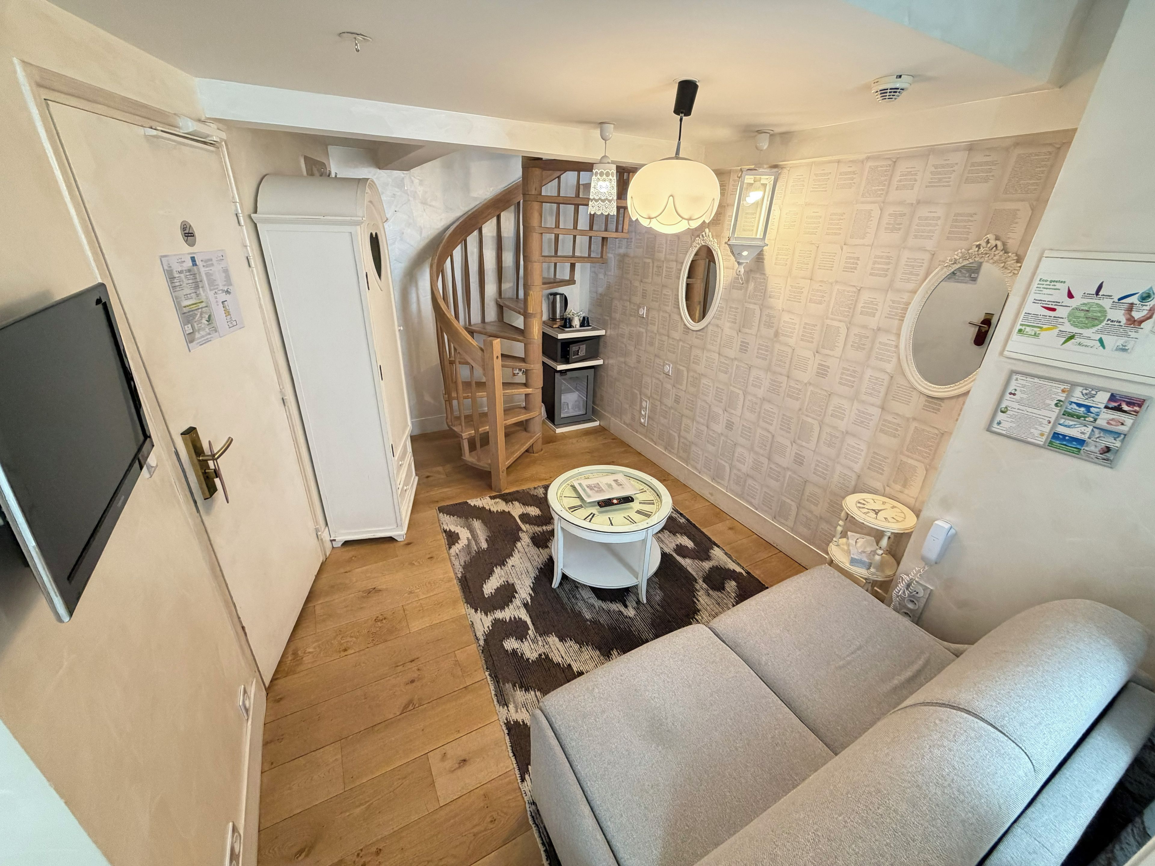 A compact living space with a sofa, a small round table, a wooden staircase, and a kitchen area.