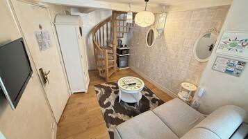 A compact living space with a sofa, a small round table, a wooden staircase, and a kitchen area.