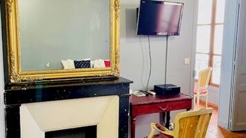 Uma sala de estar com lareira, televisão fixada na parede, escrivaninha de madeira, cadeira e tapete vermelho.