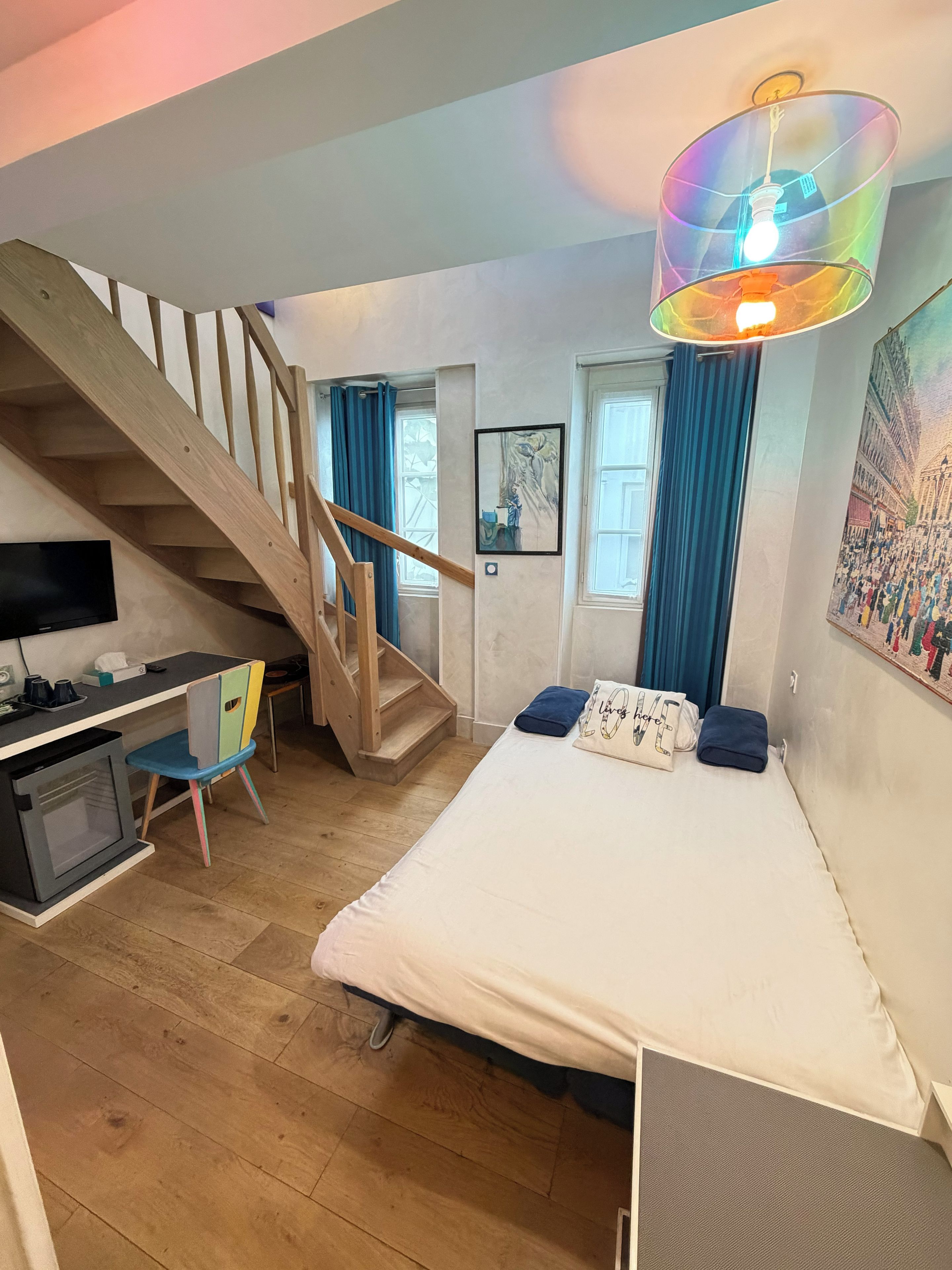 Un dormitorio con una cama, un escritorio, una silla, una escalera y un cuadro en la pared.
