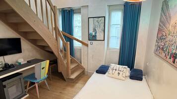 Un dormitorio con una cama, un escritorio, una silla, una escalera y un cuadro en la pared.