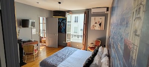 A bedroom with a bed, a desk, a chair, a television, and a balcony with a view. - Hotel le Pavillon (Paris)