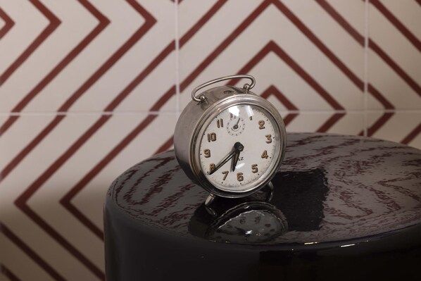 A metallic alarm clock with a white face and black numbers, placed on a reflective black surface.