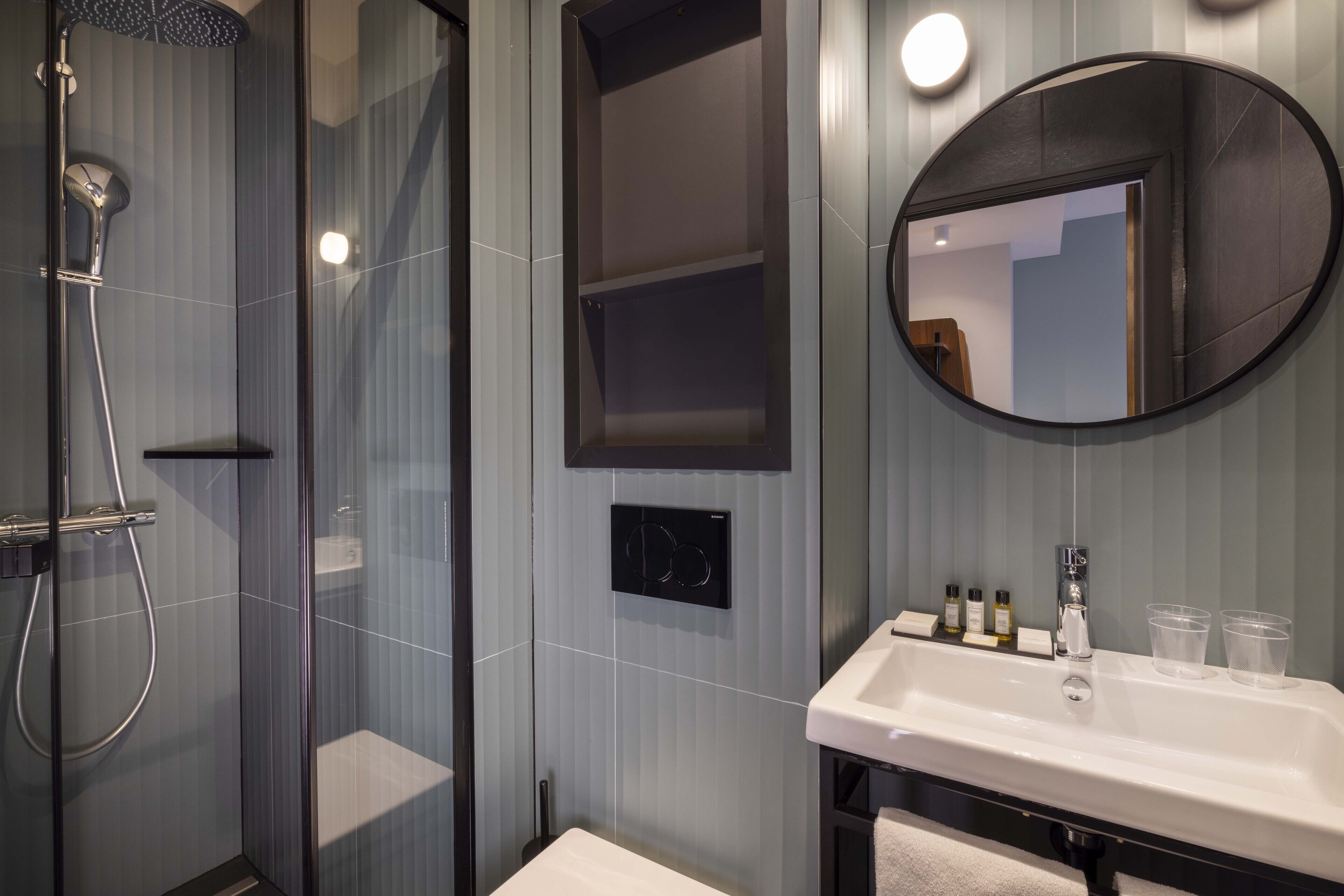 Une salle de bain moderne avec une douche à parois de verre, un lavabo blanc et un miroir rond.