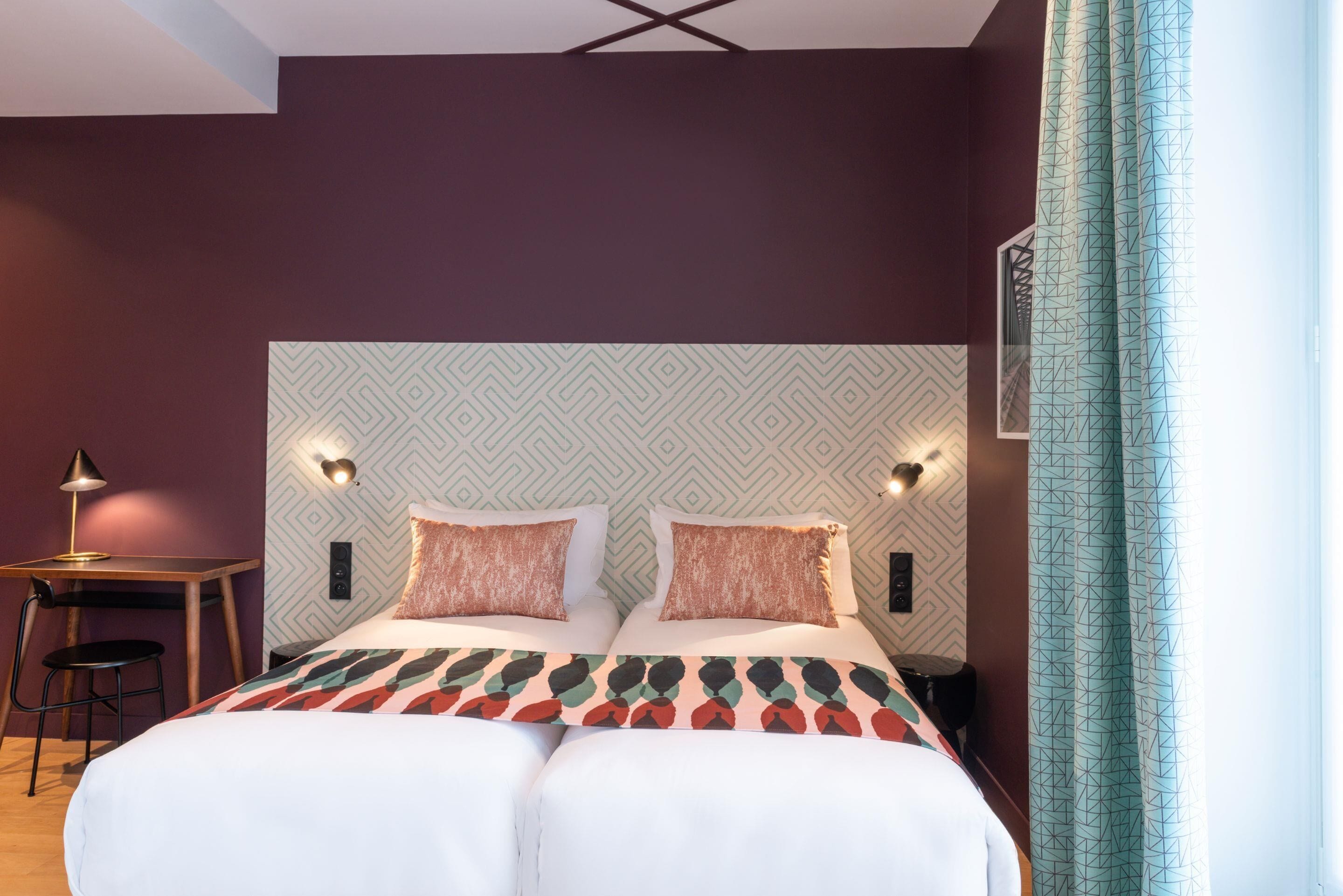 Un lit double avec une couvre-lit à motifs, deux lampes de chevet et une tête de lit ornée d’un motif géométrique.