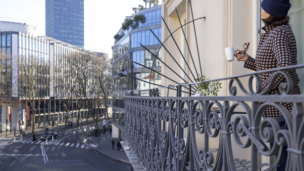 Een balkon met versierde metalen hekwerk, met uitzicht op een straat met gebouwen en bomen.