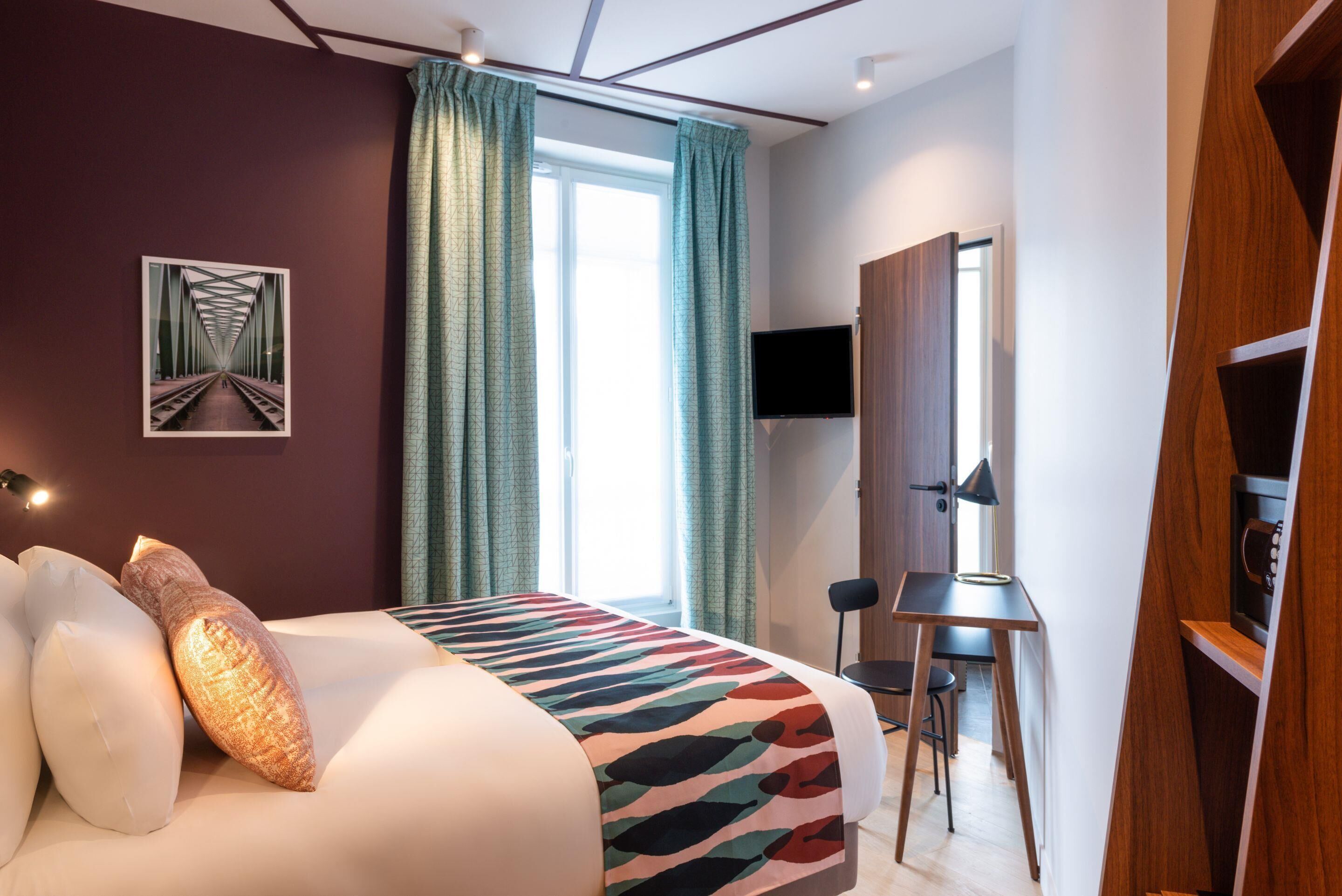 Una habitación de hotel moderna con cama, escritorio, silla, televisor y ventana con cortinas.