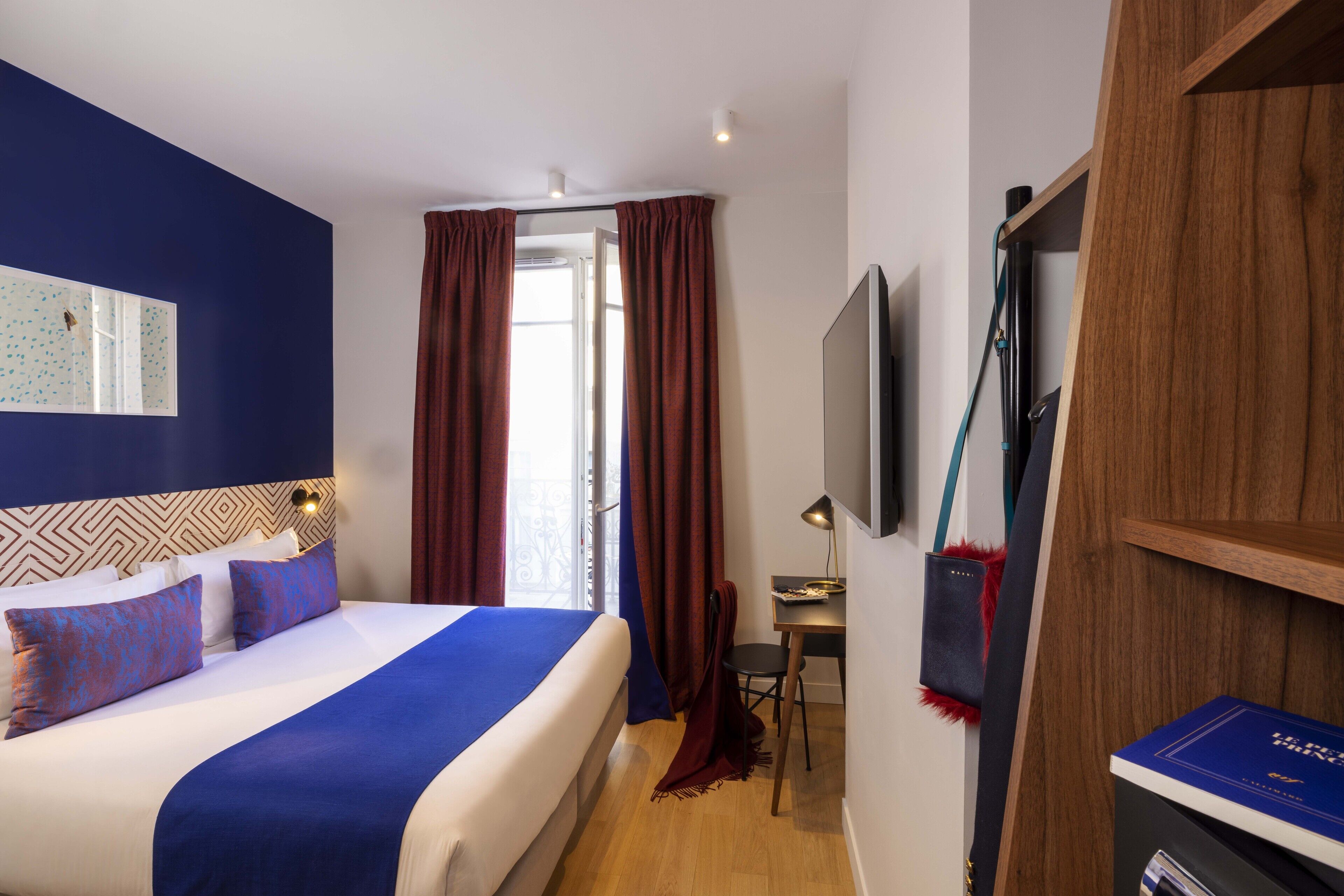 A hotel room with a large bed, a desk with a chair, a TV mounted on the wall, and a wardrobe.
