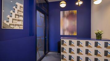 Un área de recepción con pared azul, un mostrador moderno y dos lámparas colgantes.