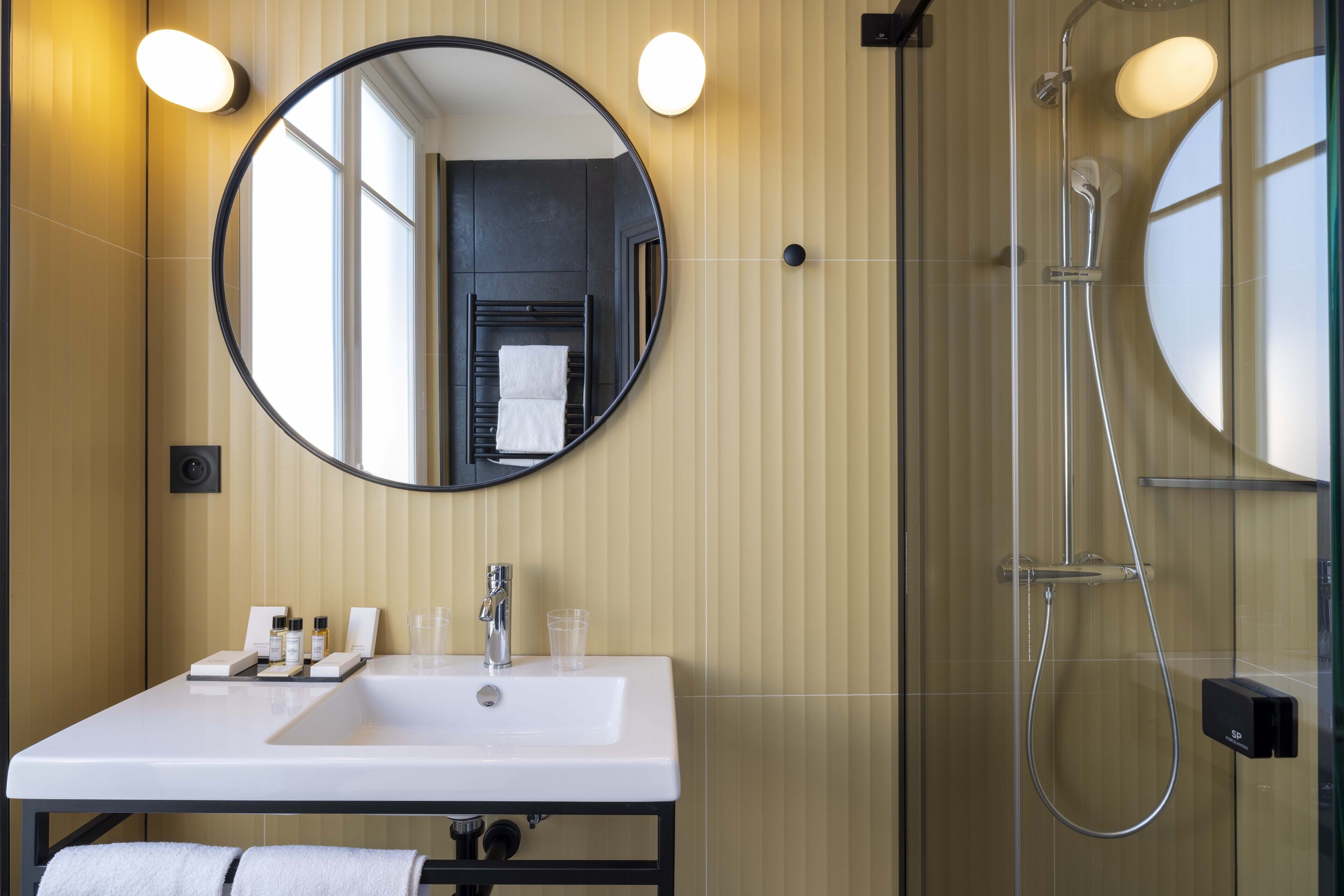 A modern bathroom with a round mirror, a white sink, and a glass-enclosed shower.