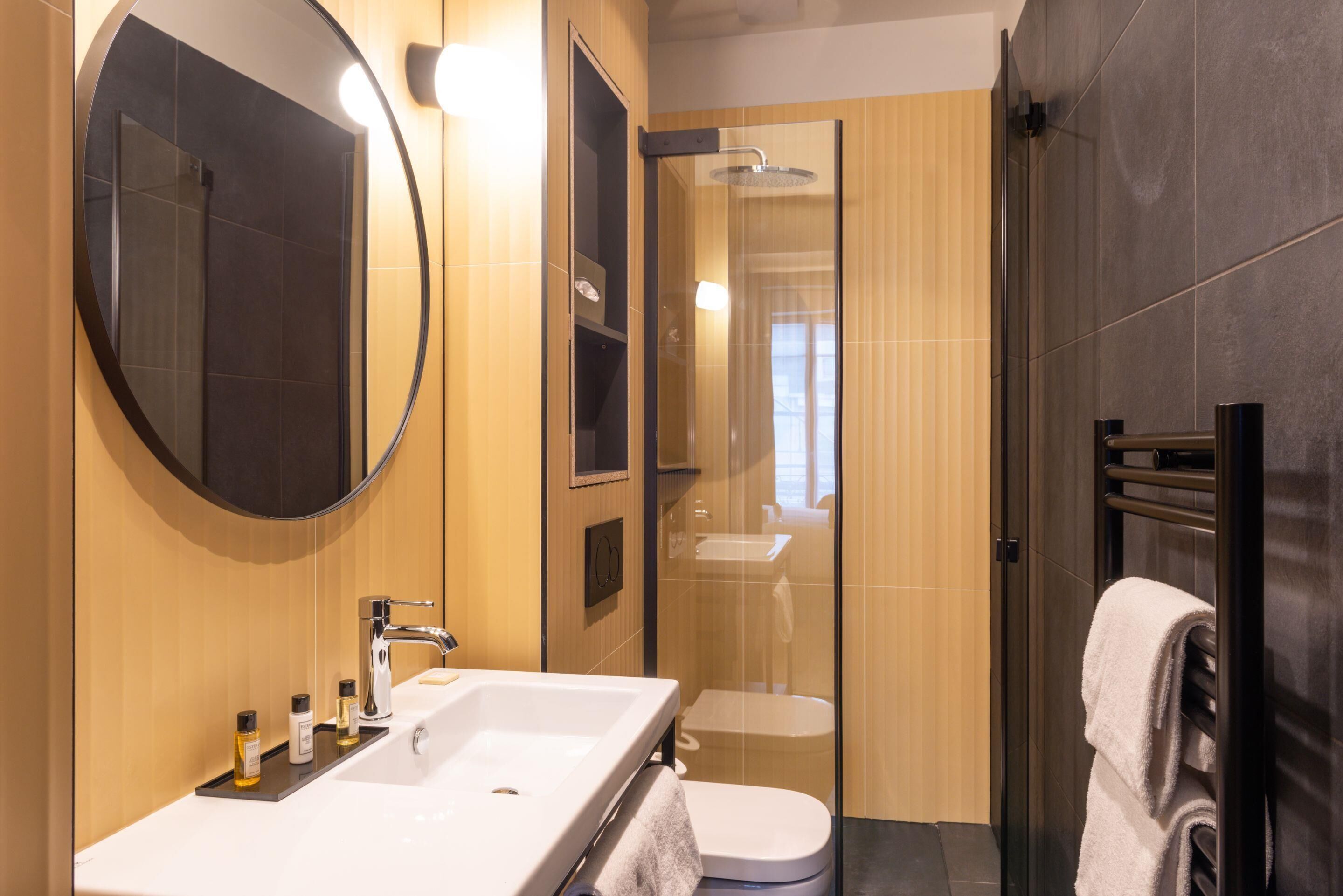 Une salle de bain moderne avec un grand miroir, un lavabo, des toilettes et une douche à parois de verre.