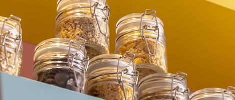 A collection of glass jars with metal clasps, containing various grains and seeds, displayed on a shelf against a yellow background.
