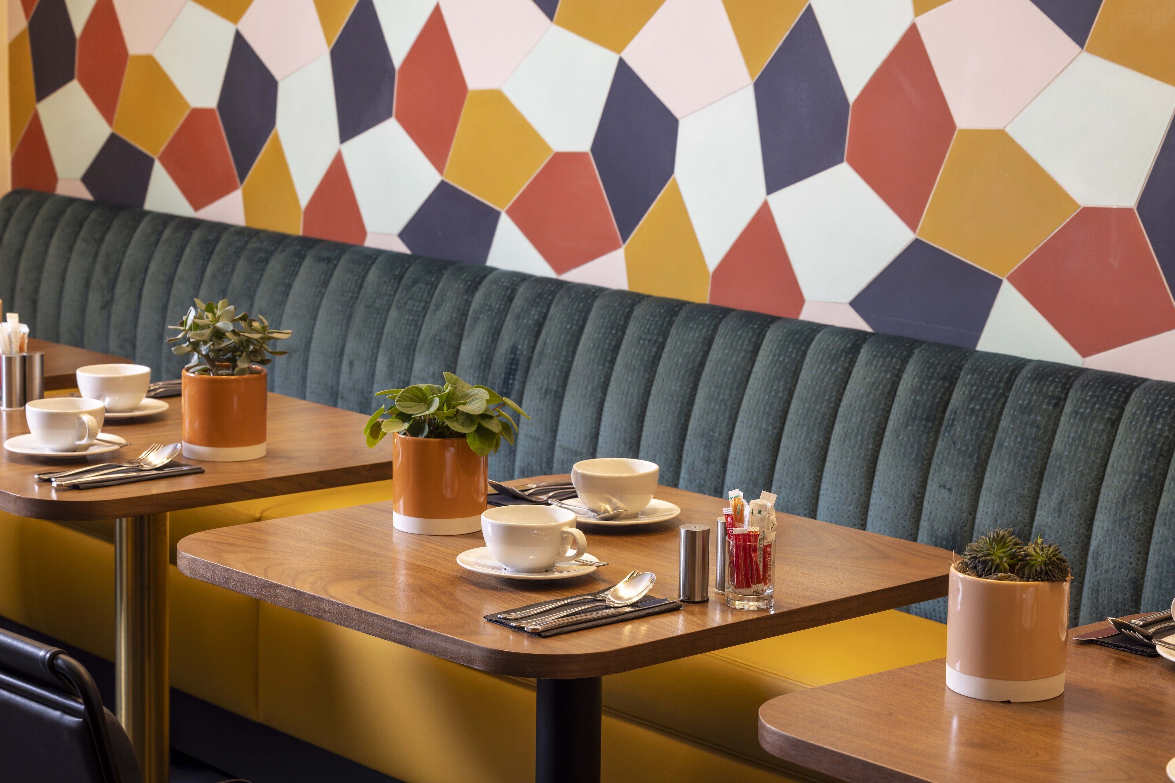 Un espace repas aménagé avec des banquettes, des tables et des plantes en pot.