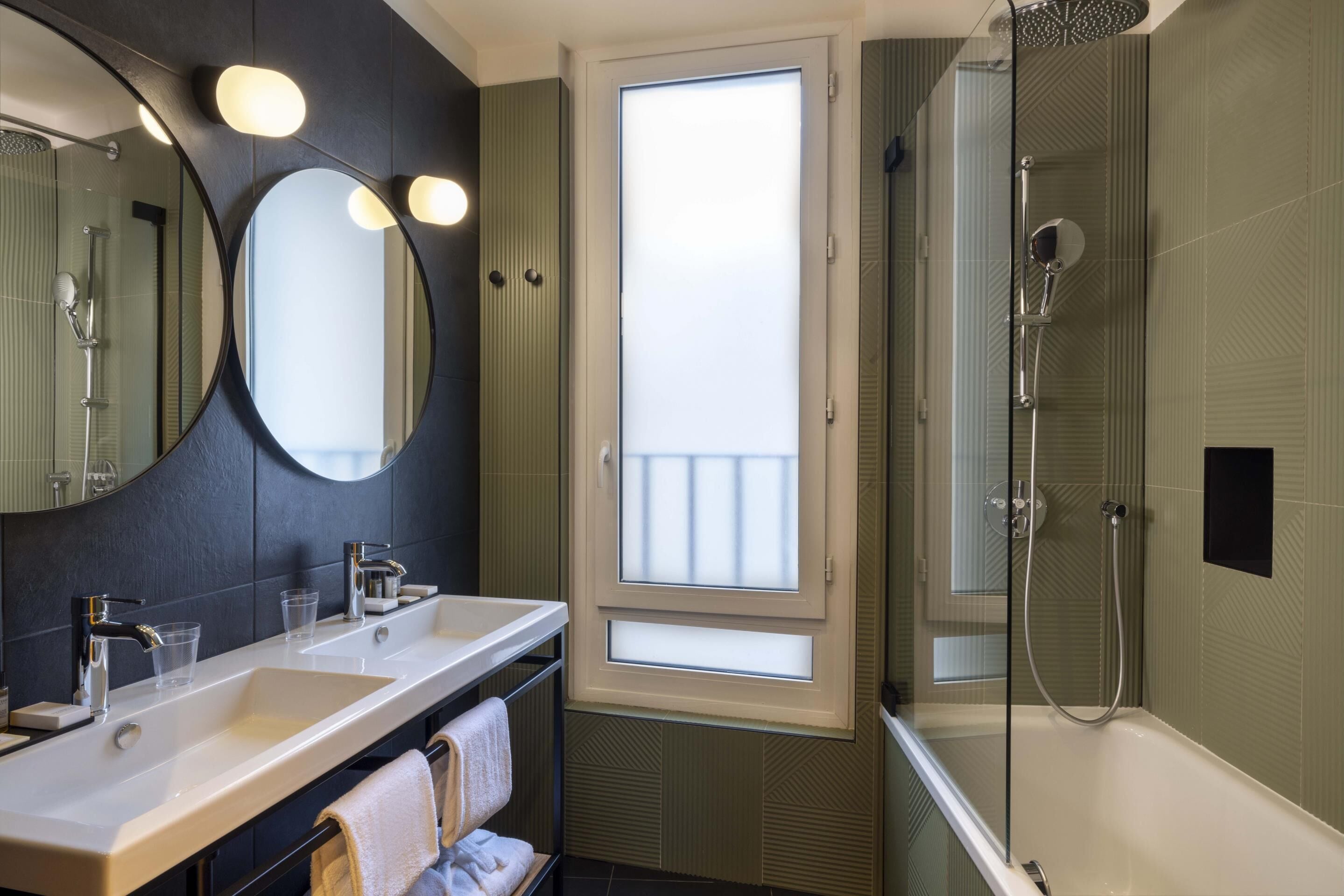 Un baño moderno con dos lavamanos, un espejo grande, ducha envuelta en vidrio y vistas a través de una ventana.