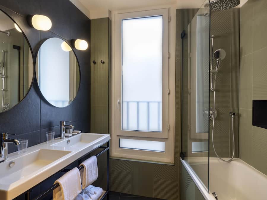 Un baño moderno con dos lavamanos, un espejo grande, ducha envuelta en vidrio y vistas a través de una ventana.