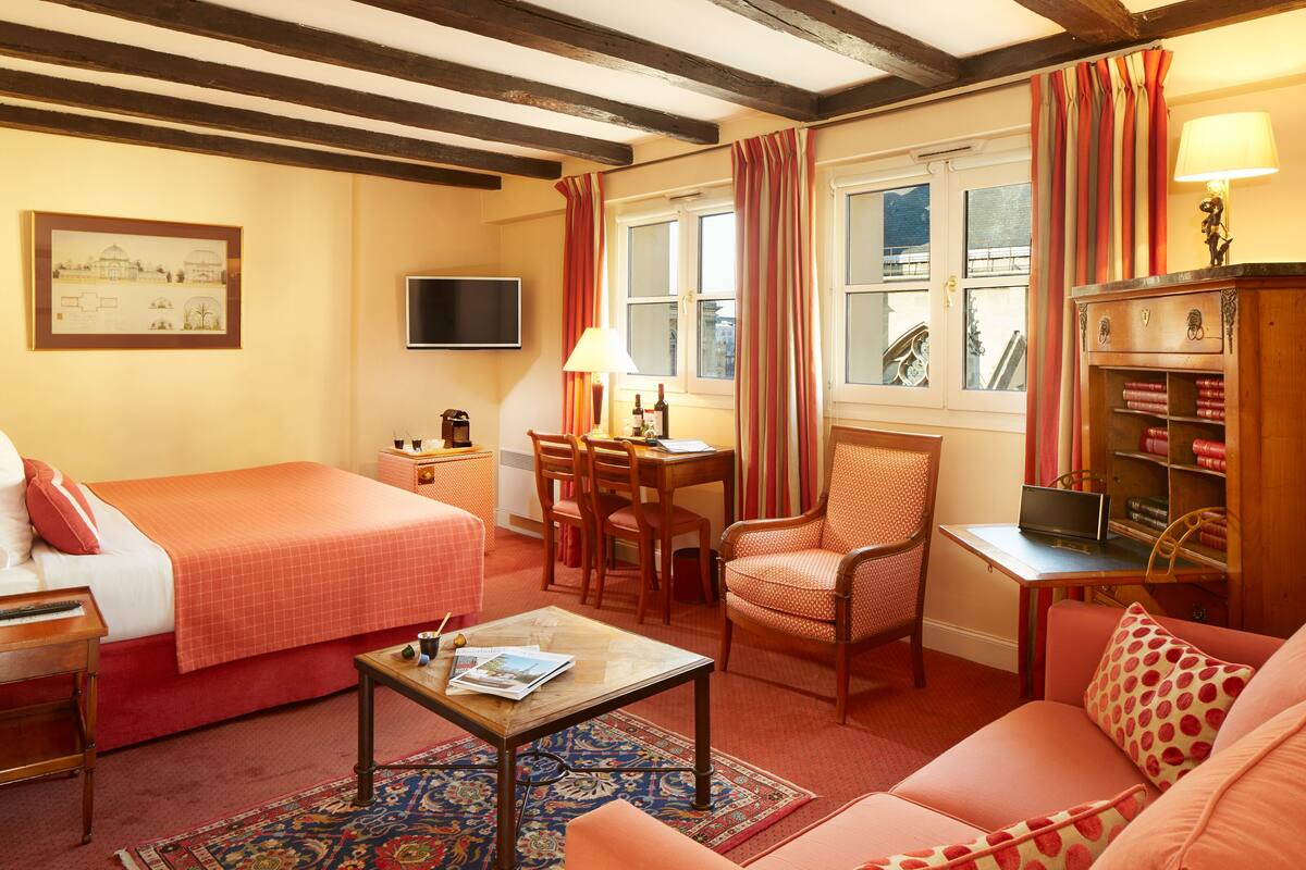 A cozy hotel room with a bed, a sofa, a desk with a lamp, a chair, and a television.