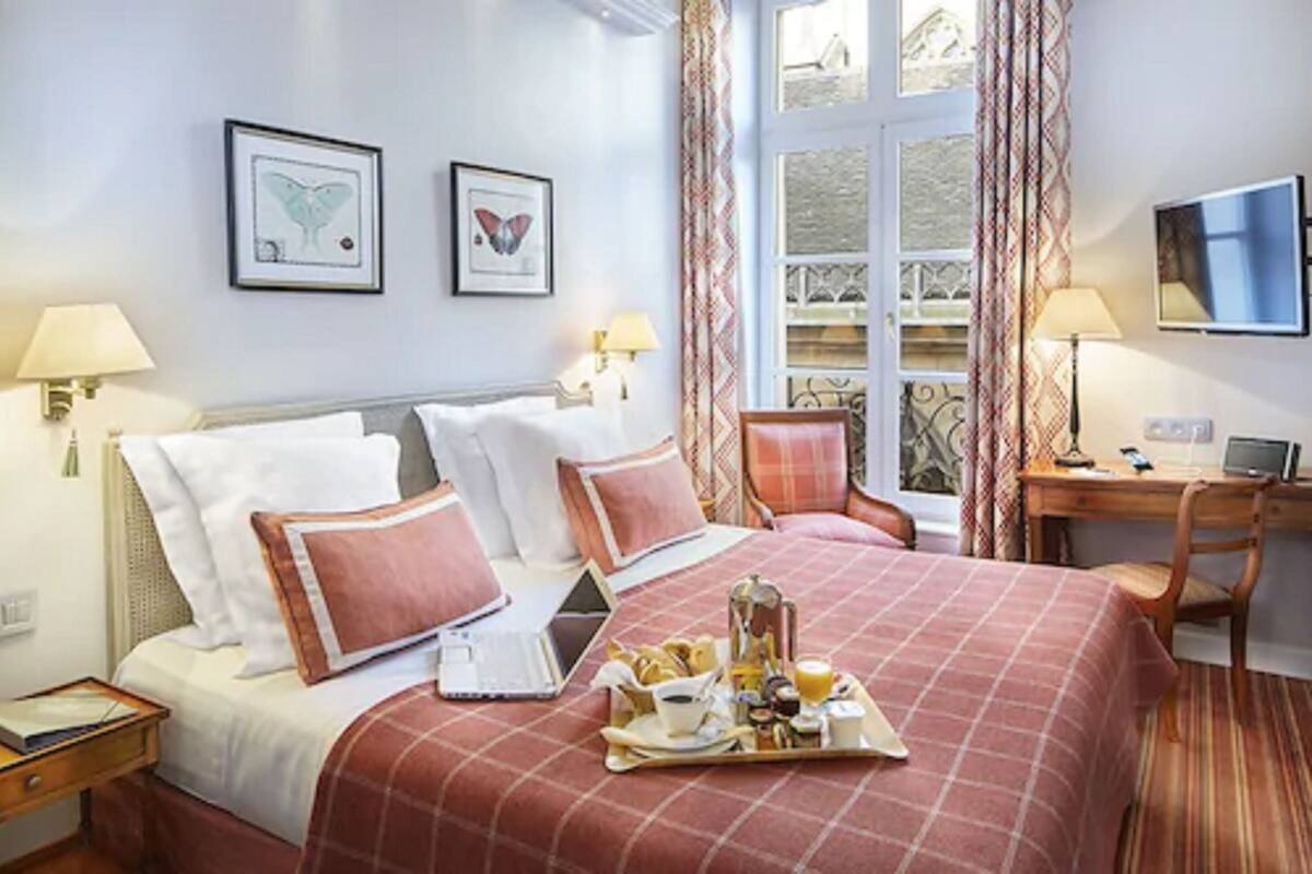 A hotel room with a bed, a desk, a chair, a tray of breakfast, and two framed pictures on the wall.