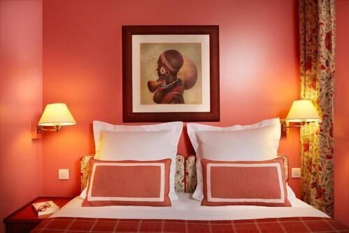A hotel room with a bed, two wall-mounted lamps, a framed picture, and a nightstand with a lamp.