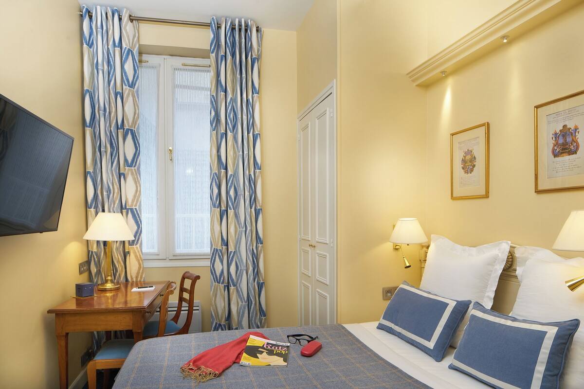 A hotel room with a bed, bedside lamps, a desk with a chair, a television, and curtains.