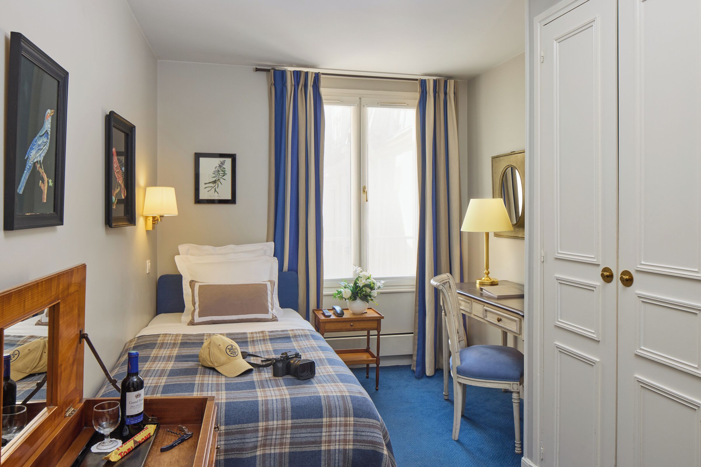 A hotel room with a bed, a desk, a chair, a dresser, and a door.