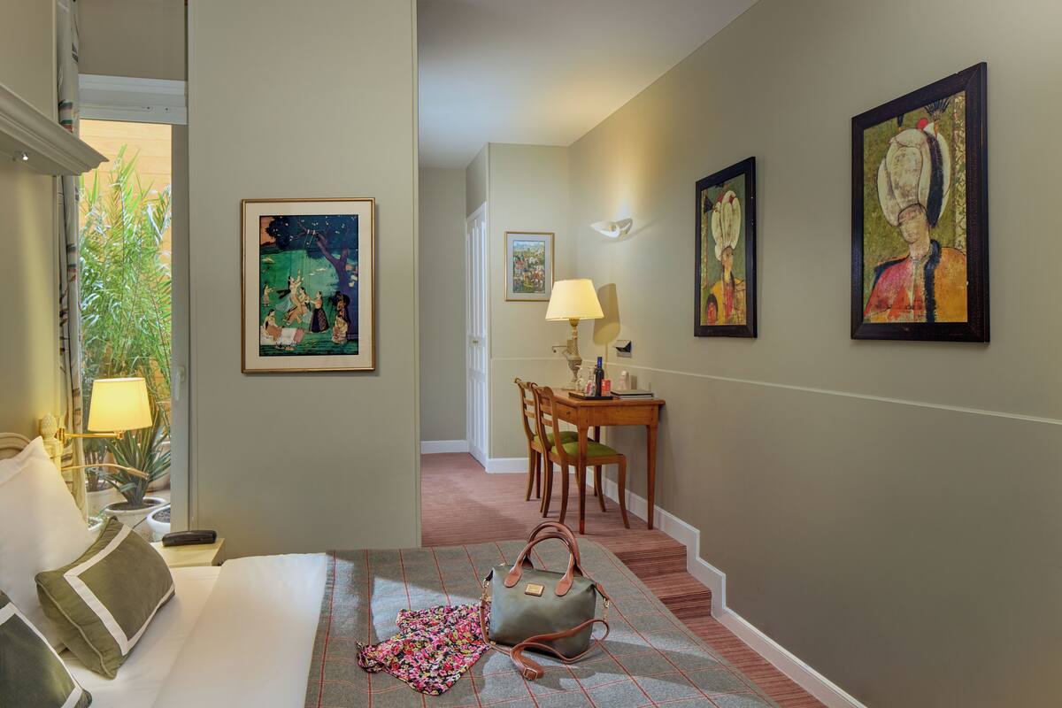 A hotel room with a bed, a desk, a chair, and artwork on the walls.