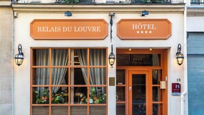 A hotel facade with large windows, a wooden door, and two signs reading "RELAIS DU LOUVRE" and "HOTEL". - Relais Du Louvre (Paris)