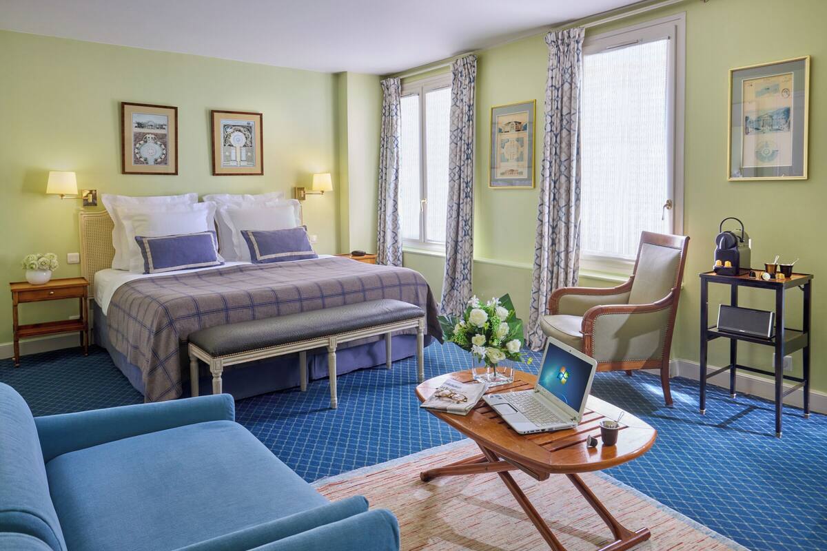 A hotel room with a bed, a desk with a laptop, a chair, and a blue sofa.