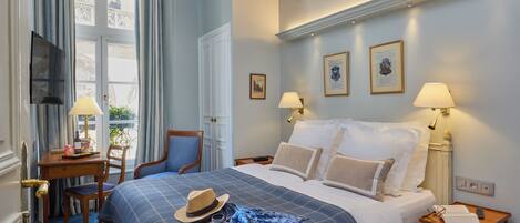 A hotel room with a bed, two bedside tables, a desk, a chair, and a window with curtains.