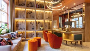 A modern interior with a sofa, ottomans, a bar area, and a wall with botanical illustrations. - Relais Du Louvre (Paris)