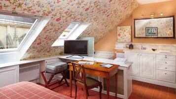 A bedroom with a sloped ceiling, a desk with a computer, a chair, a bed, and a window.