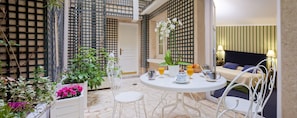 A room with a bed, a dining table with breakfast items, and a balcony with plants and a view of the street. - Hotel Beaubourg (Paris)