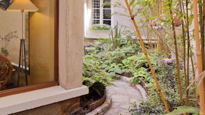 A garden pathway leading to a building with a window and a lamp. - Hotel Beaubourg (Paris)