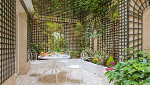 A patio with a round table and four chairs, surrounded by a lattice wall and various plants. - Hotel Beaubourg (Paris)