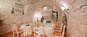 A stone-walled dining area with round tables, white chairs, and framed pictures on the walls. - Hotel Beaubourg (Paris)