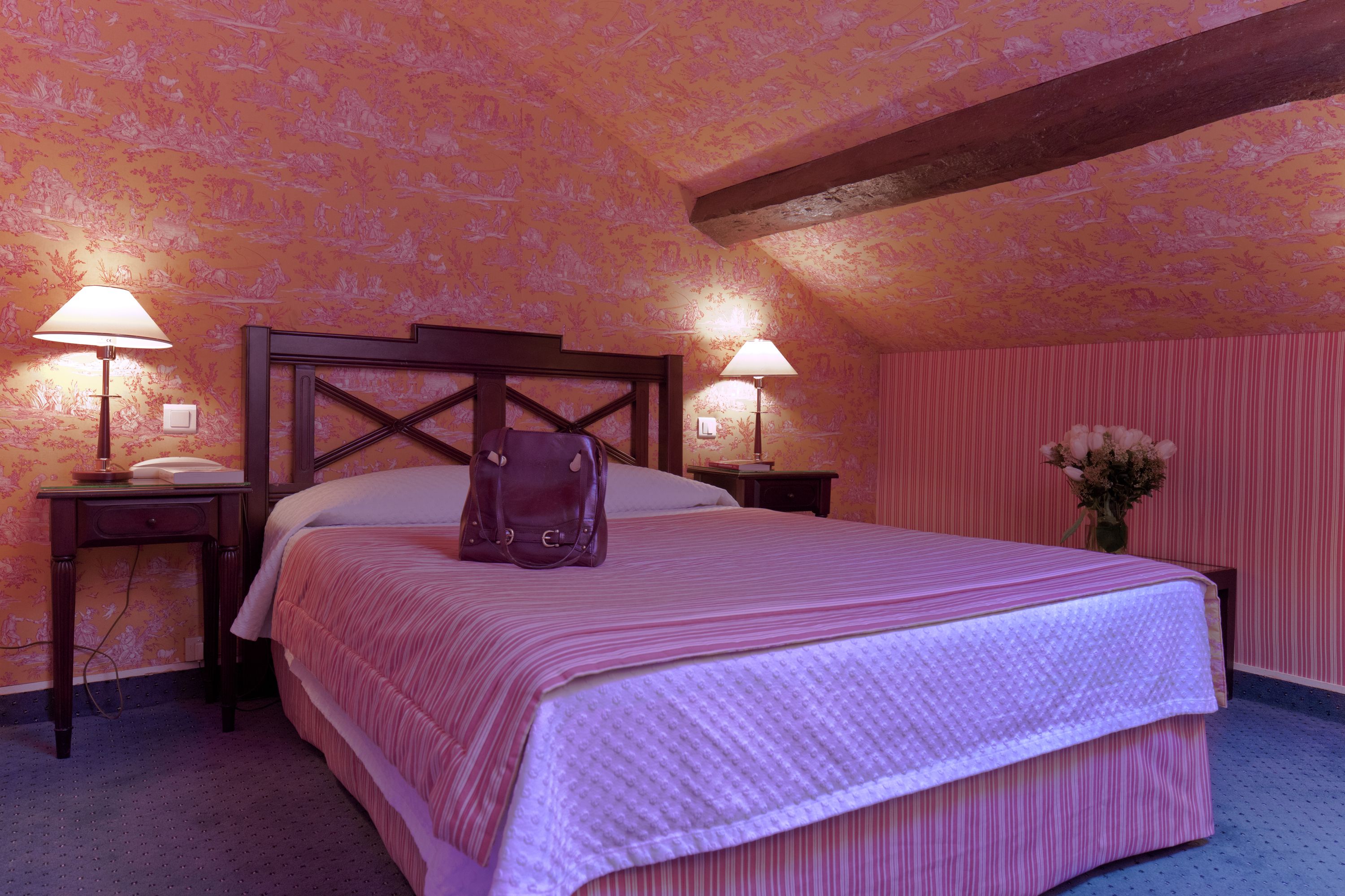 Un dormitorio con una cama grande, dos mesitas de noche con lámparas, un cabecero de madera y un estampado de flores en el papel tapiz.