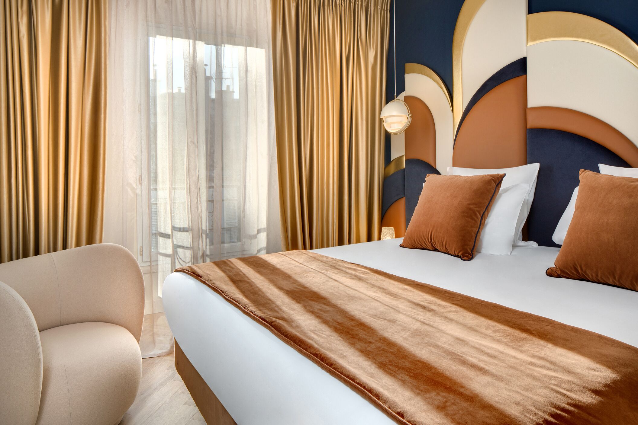 A hotel room with a large bed, beige curtains, a sofa, and a modern headboard.