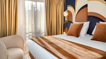 A hotel room with a large bed, beige curtains, a sofa, and a modern headboard.