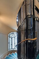 Una escalera de caracol con barandillas de metal y un pasamanos de madera, que conduce a un rellano con un vitral.