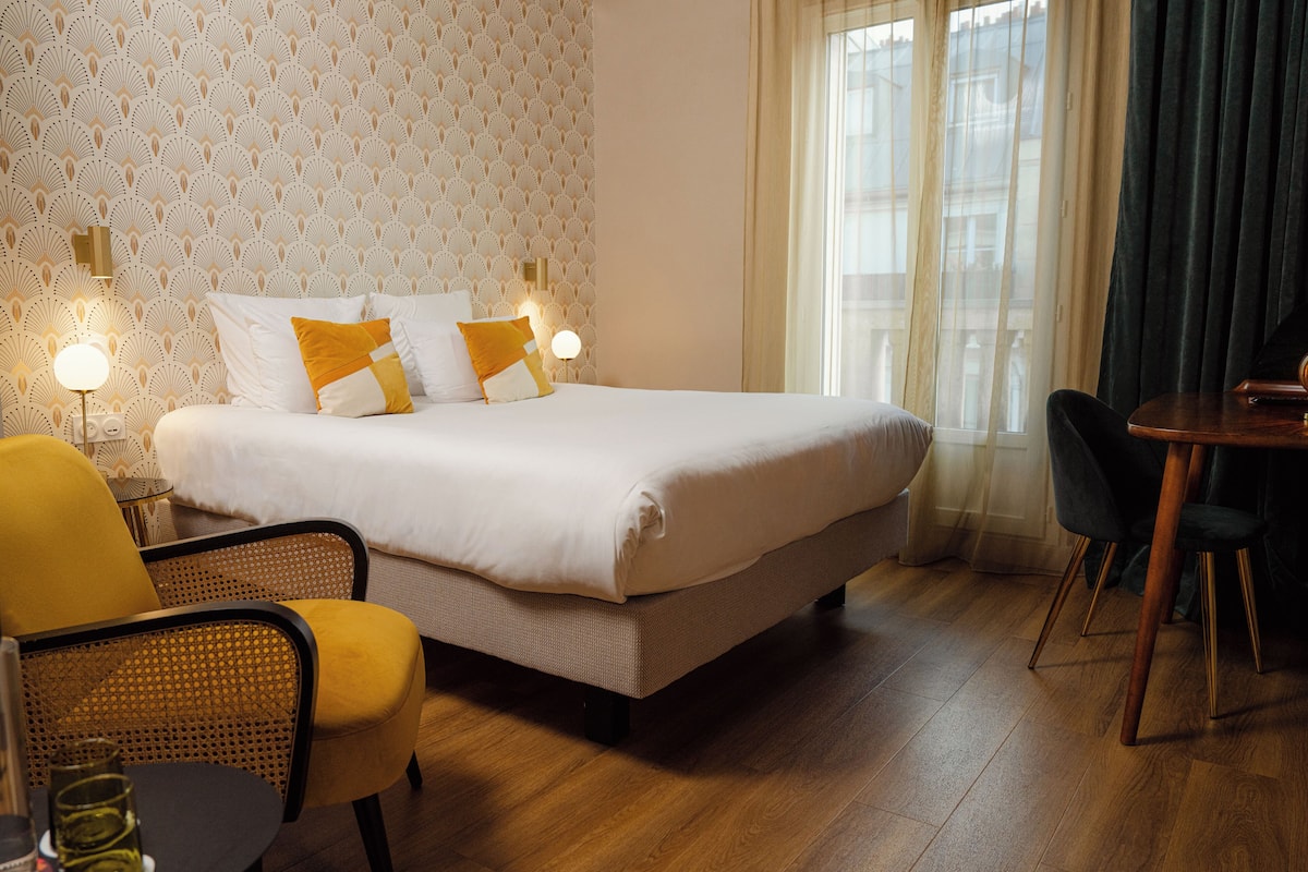 Una camera d'albergo ordinata con un letto grande, due lampade sui comodini, un tavolo da pranzo e sedie.
