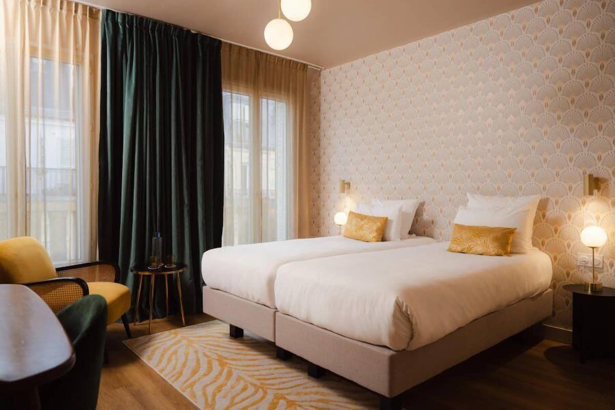 Un letto matrimoniale con due cuscini, un comodino, una sedia e un tappeto decorato in una camera d'albergo.