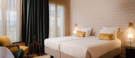 Cama doble con dos almohadas, una mesita de noche pequeña, una silla y una alfombra estampada en una habitación de hotel.