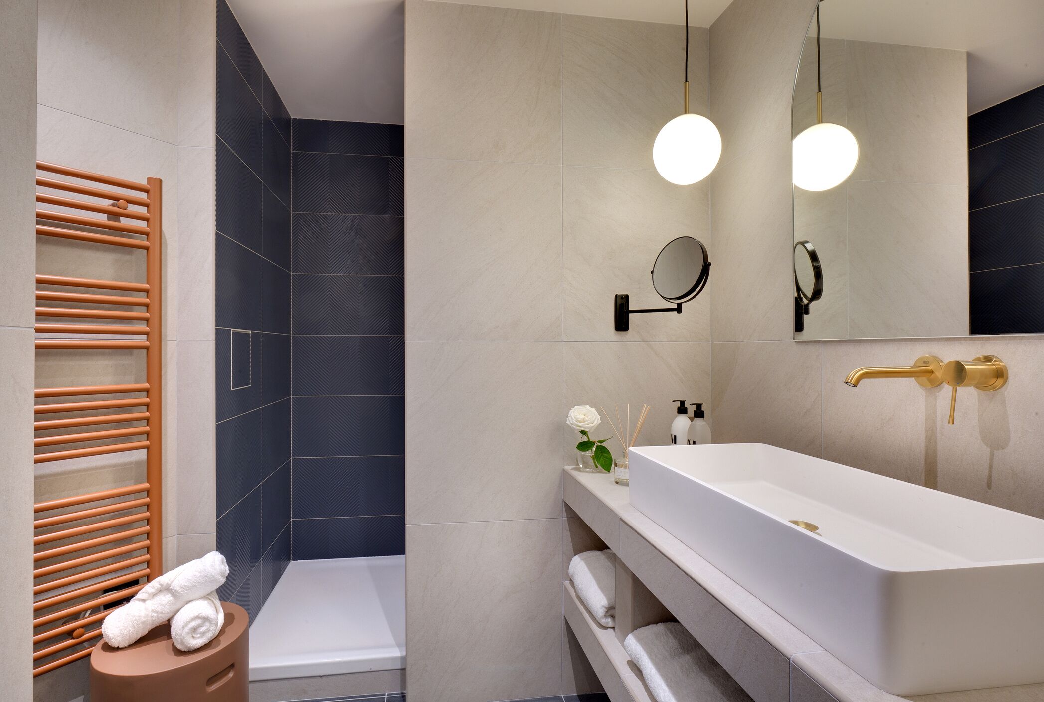 Un baño moderno con un lavamanos blanco, un espejo redondo, un perchero para toallas y una zona de ducha.