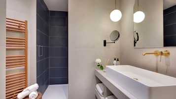 Un baño moderno con un lavamanos blanco, un espejo redondo, un perchero para toallas y una zona de ducha.