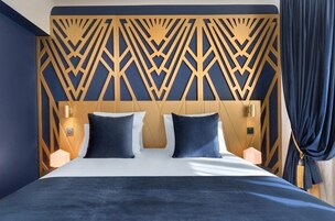 A hotel room with a geometric patterned headboard, a bed with dark bedding, and two bedside lamps.