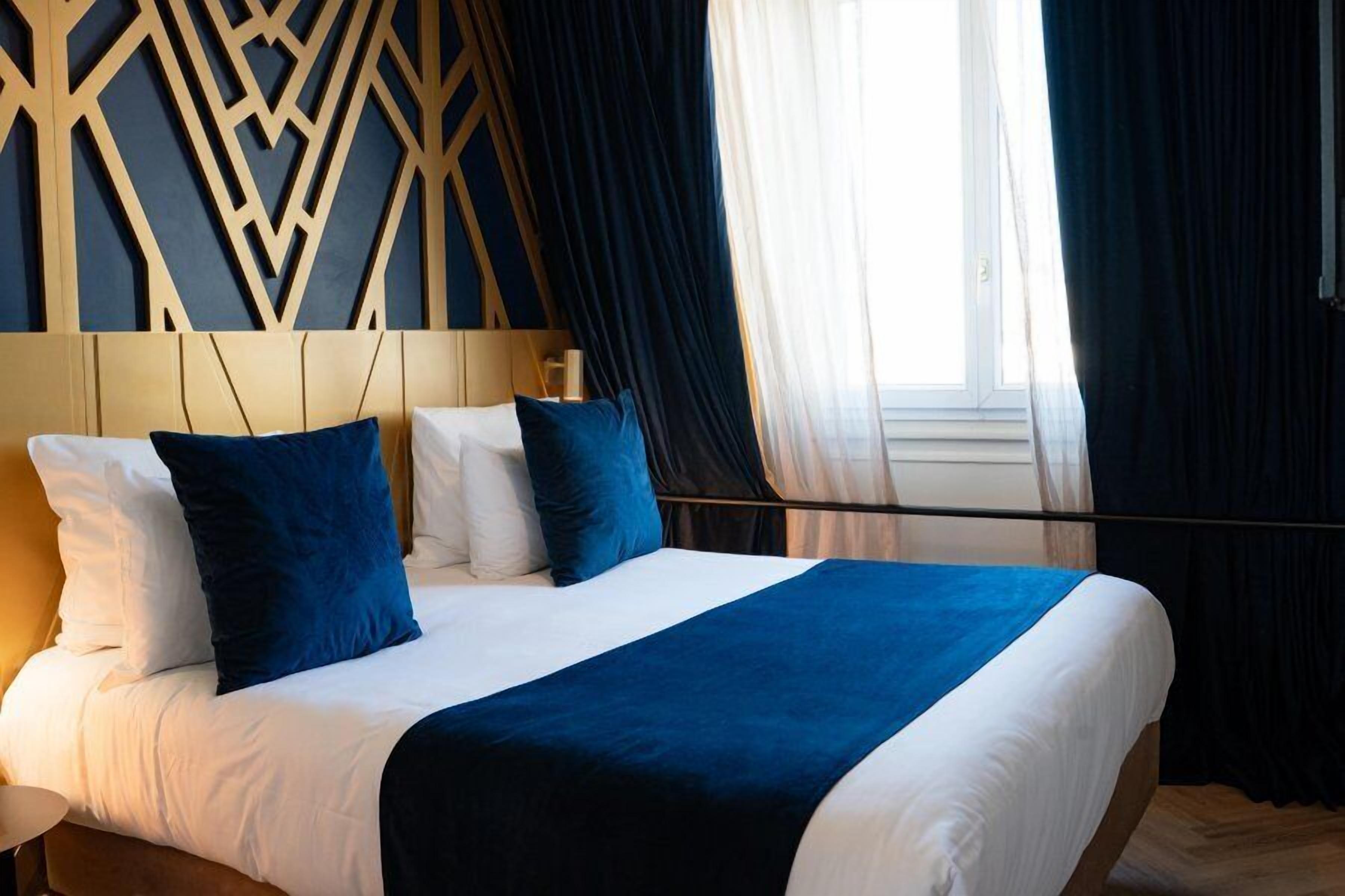 Una habitación de hotel con cama, cabecera de diseño geométrico y ventana con cortinas.