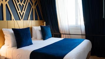 Una habitación de hotel con cama, cabecera de diseño geométrico y ventana con cortinas.