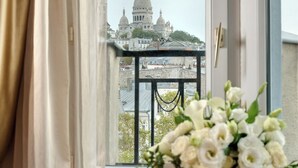 Una stanza con vista su un edificio a cupola attraverso una finestra, un vaso con fiori bianchi su un tavolino e una sedia arancione.