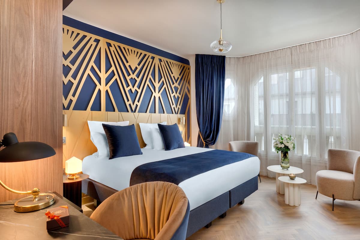 Una camera d'albergo moderna con un letto grande, due poltrone, un tavolino e un pannello decorativo al muro.