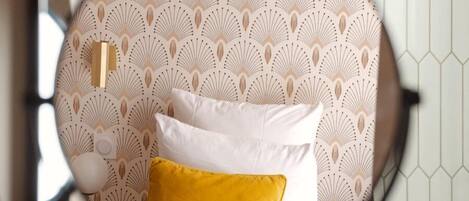 A circular mirror reflecting a bed with white and yellow pillows, a patterned wallpaper, and a hexagonal tile wall.