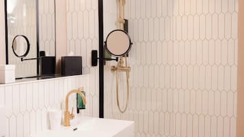 A modern bathroom with a white sink, a mirror, a handheld showerhead, and a towel rack.